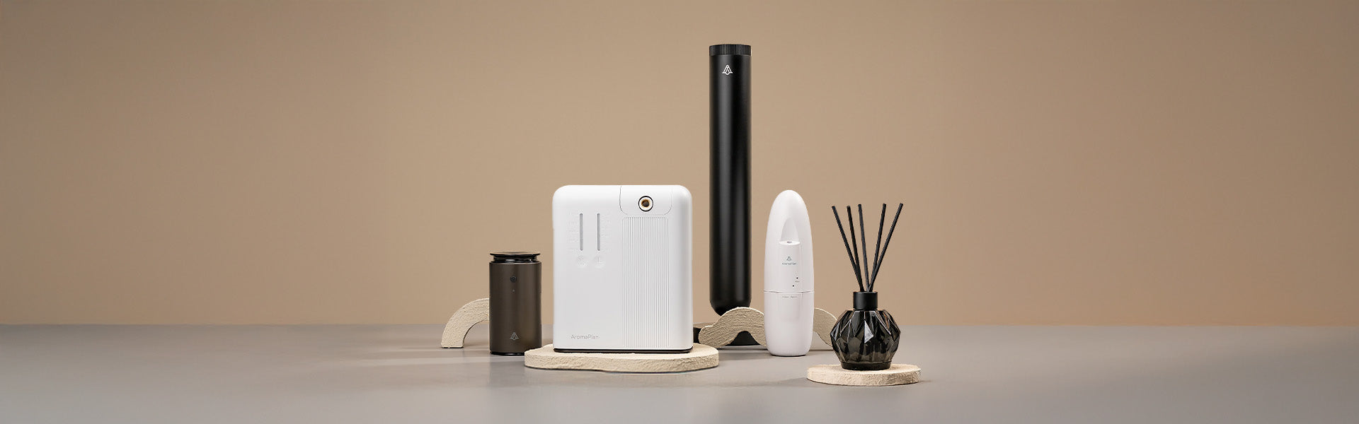 A set of four aroma diffusers with different shapes and sizes, displayed on beige stone-like stands. The background is a plain neutral beige color.