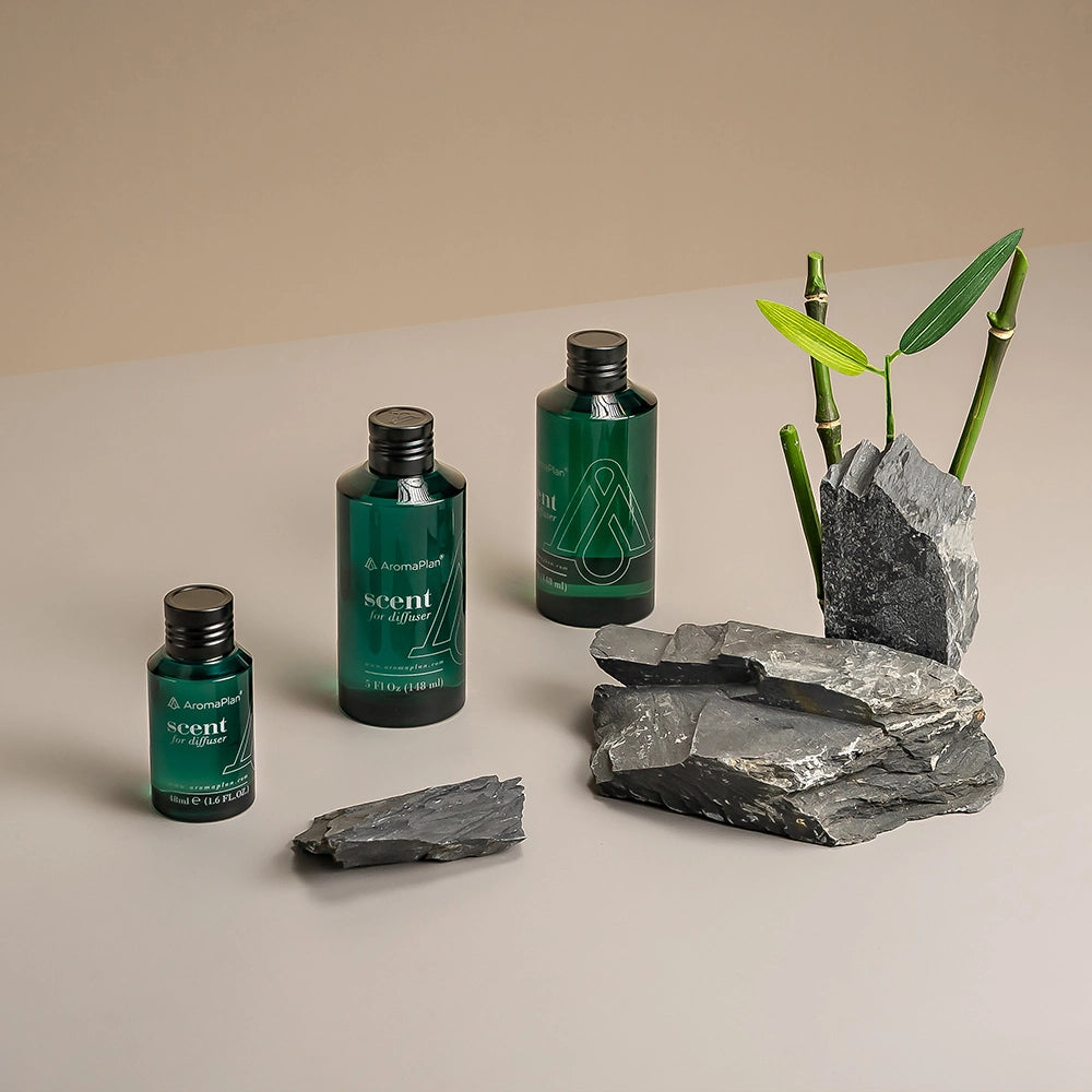 Aromatherapy scene featuring green AromaPlan scent bottles, bamboo stalks, and gray rocks on a neutral background.