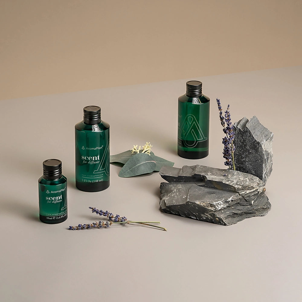 Aromatherapy scene with green AromaPlan scent bottles, purple lavender sprigs, and large gray rocks arranged on a neutral-colored background