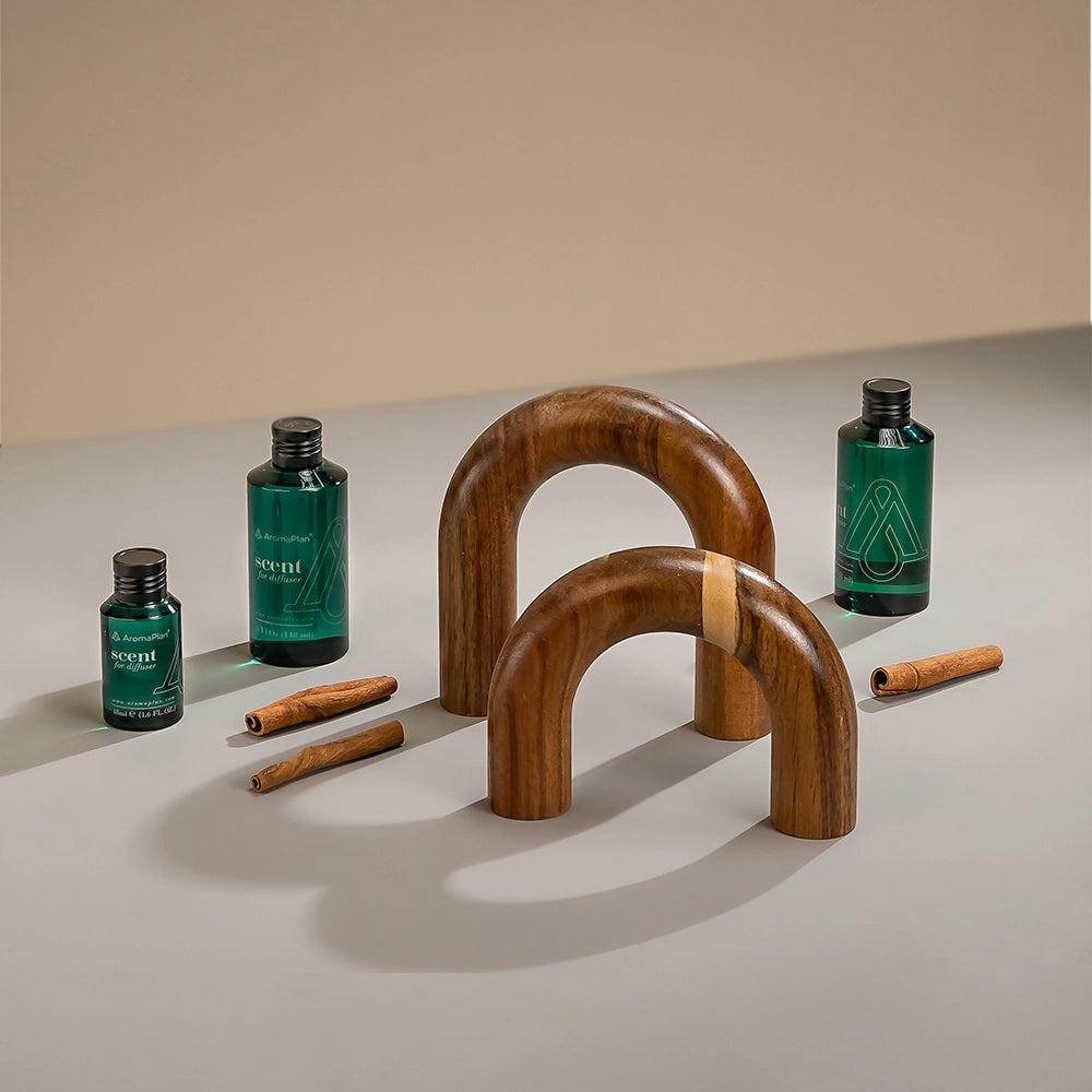 A minimalist arrangement featuring two wooden arch shapes, with two bottles of fragrance oil and cinnamon sticks placed around them. The background is a light beige tone.