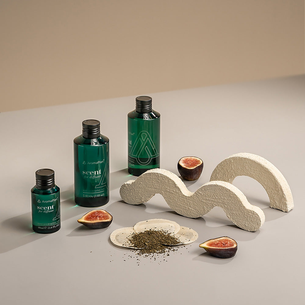 A display of AromaPlan scent diffusers with bottles of "Scent for Diffuser" surrounded by fig fruits and decorative stone shapes.